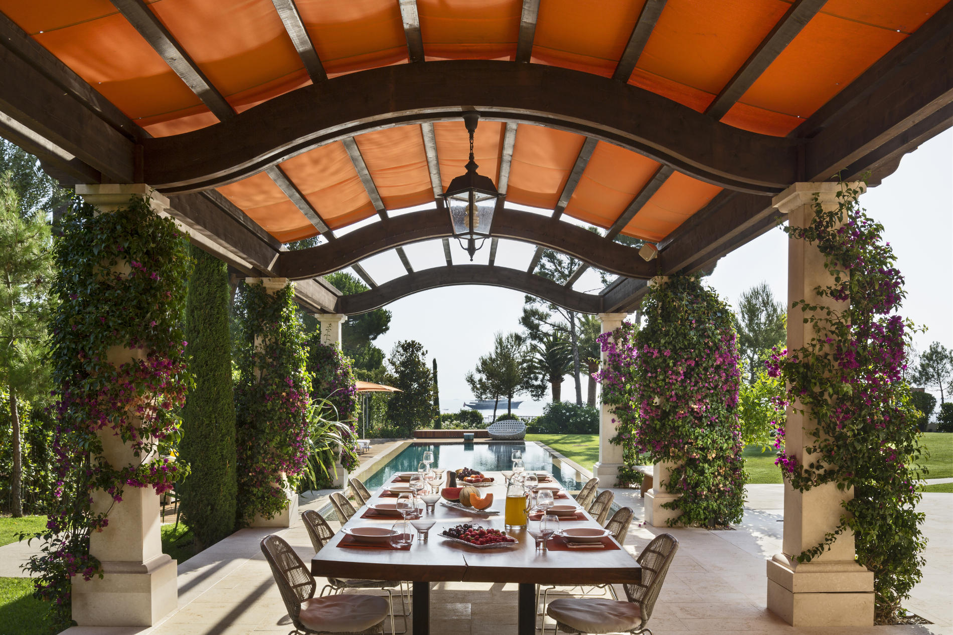 An awning-covered pergola provides a colorful, shaded space for outdoor dining and views across the pool to the Mediterranean Sea. (Photo credit: Peter Aaron/OTTO for Robert A.M. Stern Architects)